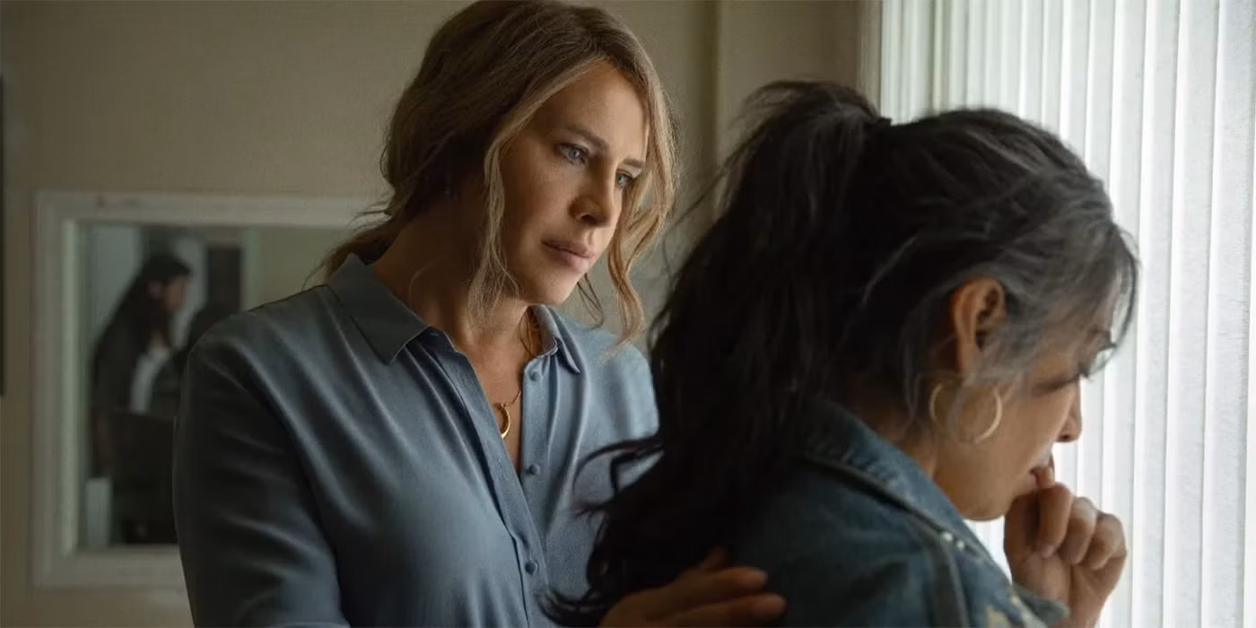 A woman is conforting another women next to a window.